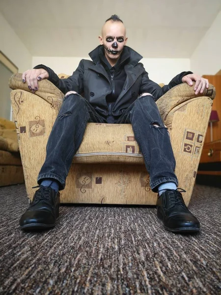 Man with scary makeup for Halloween sitting in armchair