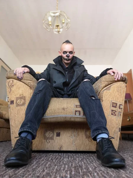 Man with scary makeup for Halloween sitting in armchair