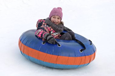 Mutlu küçük kız tepeden kayıyor karlı bir parkta