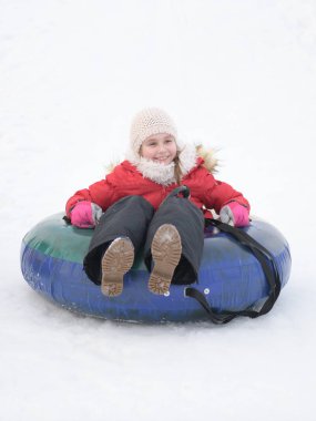 Mutlu küçük kız tepeden kayıyor karlı bir parkta