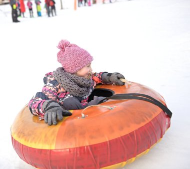 Mutlu küçük kız tepeden kayıyor karlı bir parkta