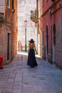 Venedik, İtalya - 25 Eylül 2016: Siyah elbiseli ve siyah şapkalı genç kadın Venedik'te sokakta yürüyor. 