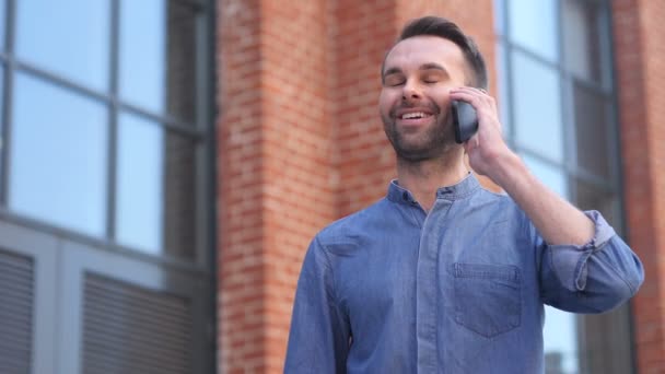 Mann telefoniert, während er vor Bürogebäude steht und diskutiert — Stockvideo