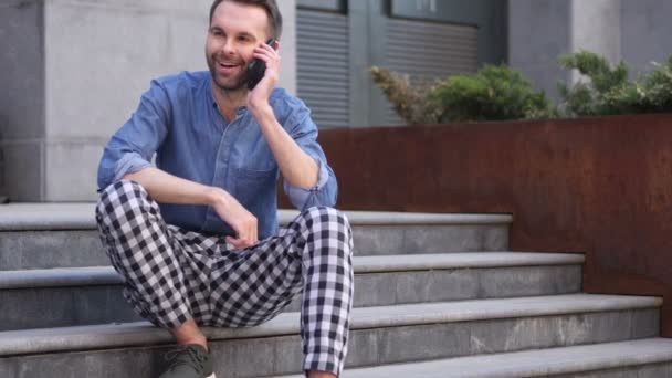 Телефонная беседа, мужчина на вызове, сидя на лестнице снаружи здания — стоковое видео