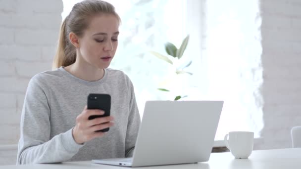 在笔记本电脑上工作时使用智能手机的年轻妇女 — 图库视频影像