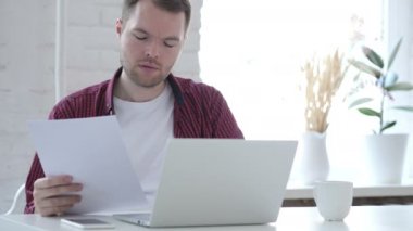 Genç adam okuma belgeleri ve çalışma üstünde Laptop