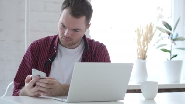 Junger Mann Benutzt Smartphone Bei Der Arbeit Laptop — Stockvideo