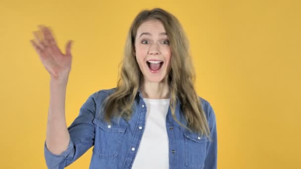 若いかわいらしい黄色の背景で歓迎に手を振っている女の子 — ストック動画
