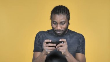 Sarı arka plan üzerinde izole Smartphone oyun oynamak casual Afrika adam
