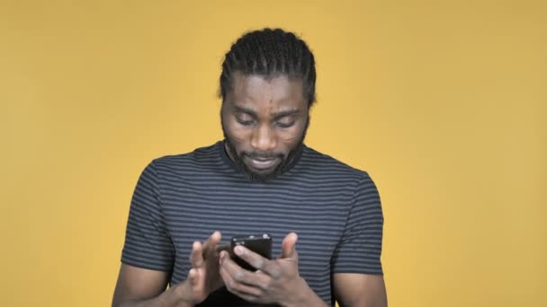 在黄色背景中使用隔离的智能手机时 在休克中的休闲非洲男人 — 图库视频影像