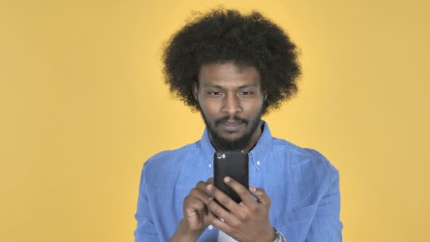 アフリカ系アメリカ人男は 黄色の背景にスマート フォンを使用している間成功のための興奮 — ストック動画