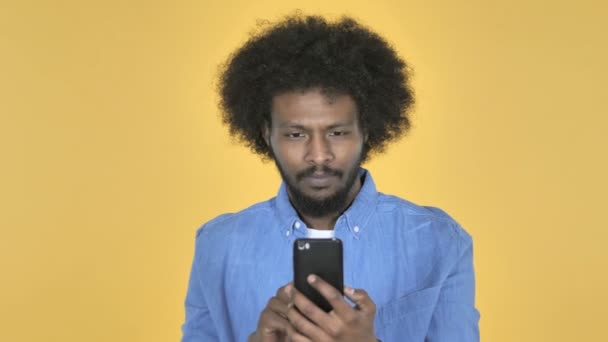 Afro Amerikan Adam Sarı Zemin Üzerine Smartphone Kullanarak Süre Şokta — Stok video