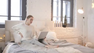 Genç kızla yatakta dizüstü bilgisayar üzerinde çalışan sırt ağrısı