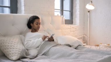 Genç Afrikalı kız kullanma Smartphone yatakta dinlenirken yaparken