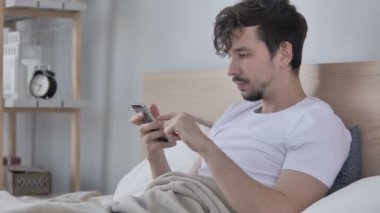 Adam akıllı telefon kullanarak Lying yatakta tarafında ise