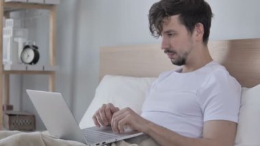 Mutlu adam kutluyor başarı kullanarak Laptop süre yatakta