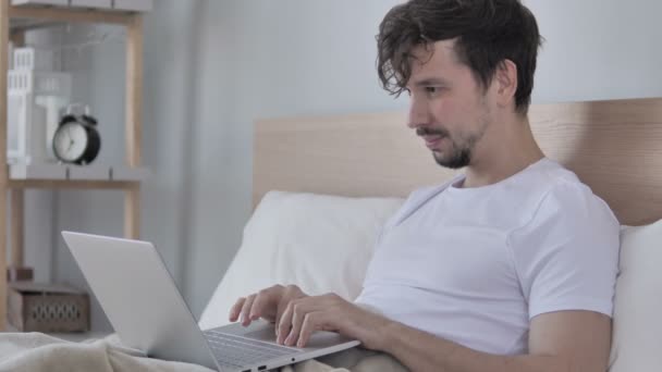 ヘソでベッドで横になっている興奮している男がオンライン ビデオ チャット — ストック動画