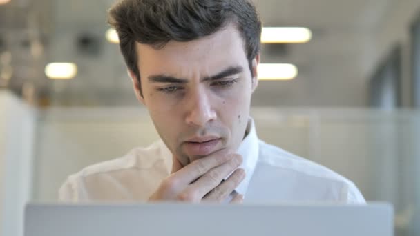 Pensant jeune homme d'affaires travaillant sur ordinateur portable, vue frontale — Video