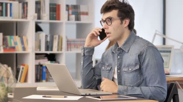 Hombre creativo hablando por teléfono y trabajando en el ordenador portátil — Vídeos de Stock