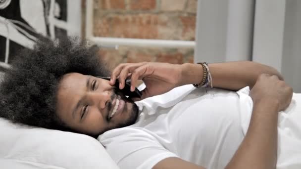 Африканский мужчина разговаривает по телефону, лежа в кровати — стоковое видео