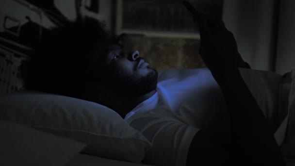 Hombre africano escribiendo mensaje en el teléfono en la cama por la noche — Vídeos de Stock