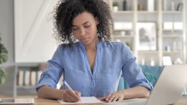 Afrikansk kvinna skriver på papper på jobbet — Stockvideo