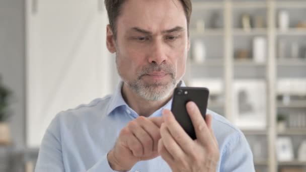 Hombre de negocios de edad avanzada reaccionando a la pérdida mientras usa el teléfono inteligente — Vídeo de stock