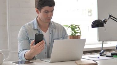 Akıllı telefon ve dizüstü bilgisayar kullanan genç adam