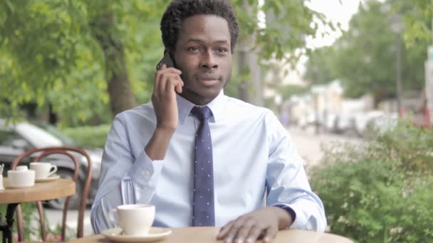 Empresario africano hablando por teléfono, sentado en el café al aire libre — Vídeos de Stock