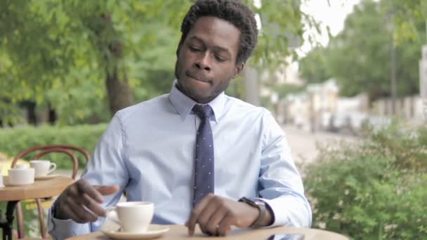 Esperando a un hombre de negocios africano tomando café en el café al aire libre y comprobando el tiempo — Vídeos de Stock