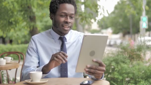 Chat vidéo en ligne sur tablette par un homme d'affaires africain, assis dans un café en plein air — Video