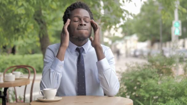 Kopfschmerzen, gestresster afrikanischer Geschäftsmann sitzt im Café — Stockvideo
