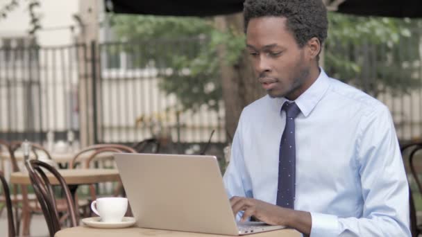 Căscatul african de afaceri lucrează pe laptop în cafeneaua în aer liber — Videoclip de stoc