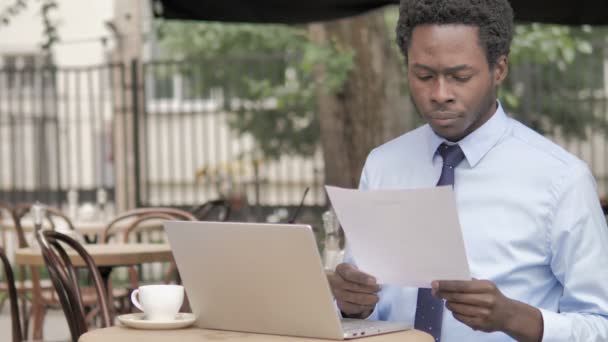 屋外カフェに座りながらドキュメントを読むアフリカのビジネスマン — ストック動画