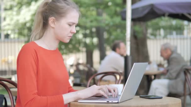 Jonge vrouw werkt op een laptop en koffie drinken zittend in cafe terras — Stockvideo