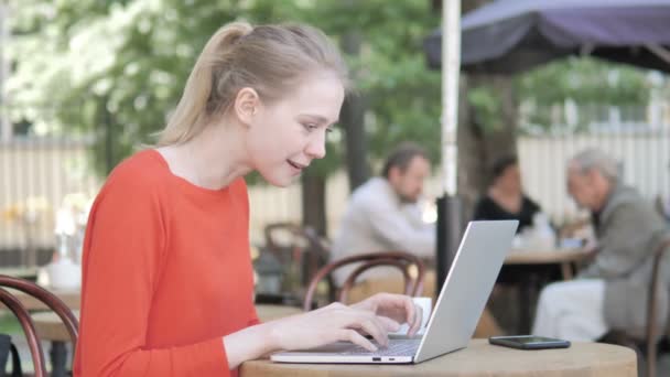 Junge Frau feiert auf Laptop auf Caféterrasse — Stockvideo