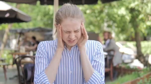 Gespannen jonge vrouw met hoofdpijn zittend in cafe terras — Stockvideo