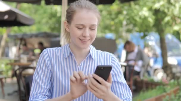 Junge Frau sitzt mit Smartphone auf Caféterrasse — Stockvideo