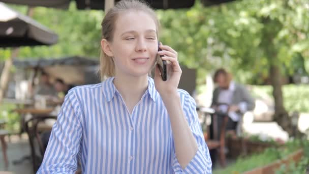 Телефон розмови молода жінка, сидячи в кафе тераса — стокове відео