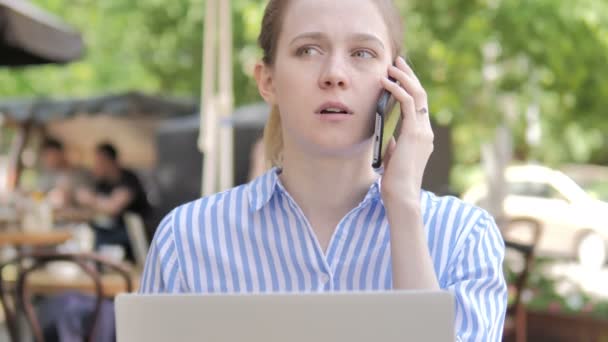 Молодая женщина разговаривает по телефону, сидя в кафе Терраса — стоковое видео