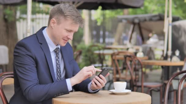 Uomo d'affari seduto all'aperto che celebra i risultati su Smartphone — Video Stock