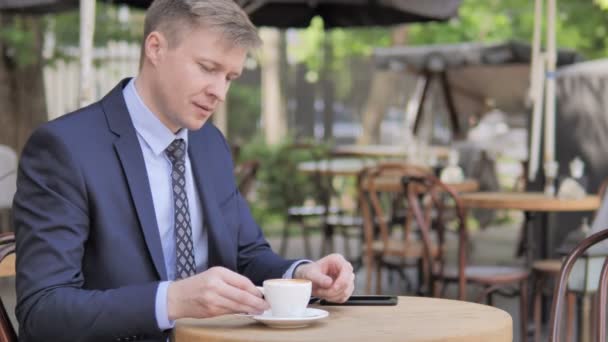 Uomo d'affari che beve caffè mentre si siede nel caffè all'aperto — Video Stock