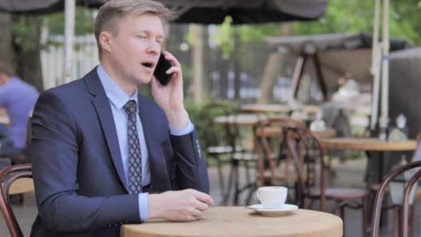 Uomo d'affari che parla al telefono mentre si siede nel caffè all'aperto — Video Stock