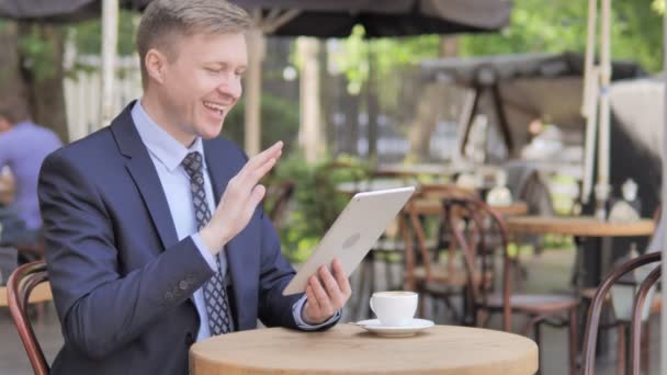 Online-Video-Chat auf dem Tablet von Geschäftsmann, sitzt im Café im Freien — Stockvideo