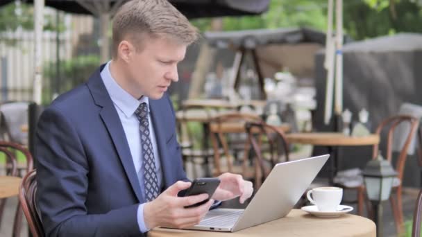 Empresario usando Smartphone y Laptop en Café al aire libre — Vídeos de Stock