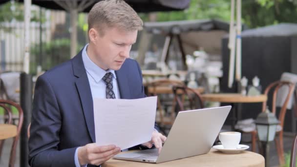 Geschäftsmann liest Vertrag und nutzt Laptop im Café — Stockvideo