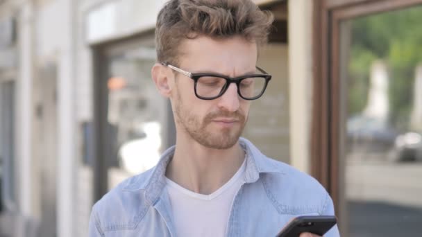 Casual ung man pratar på telefon medan stående utomhus — Stockvideo