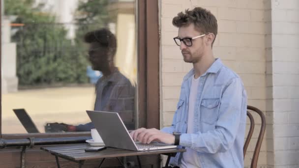 Νέος άντρας γιορτάζει την επιτυχία στο φορητό υπολογιστή, καθιστός υπαίθριος — Αρχείο Βίντεο