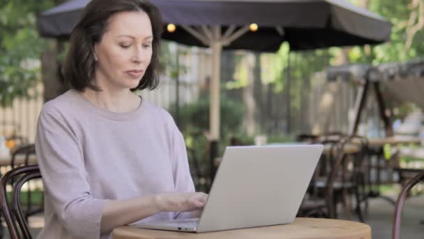 Кашель стара жінка працює на ноутбуці у відкритому кафе — стокове відео