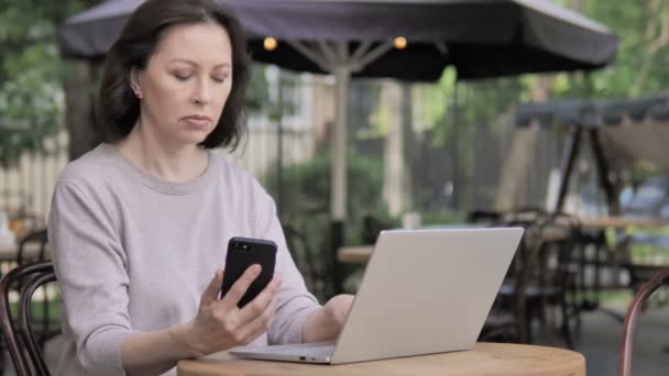 Mujer vieja usando Smartphone y Laptop, Sentado en Café al aire libre — Vídeos de Stock